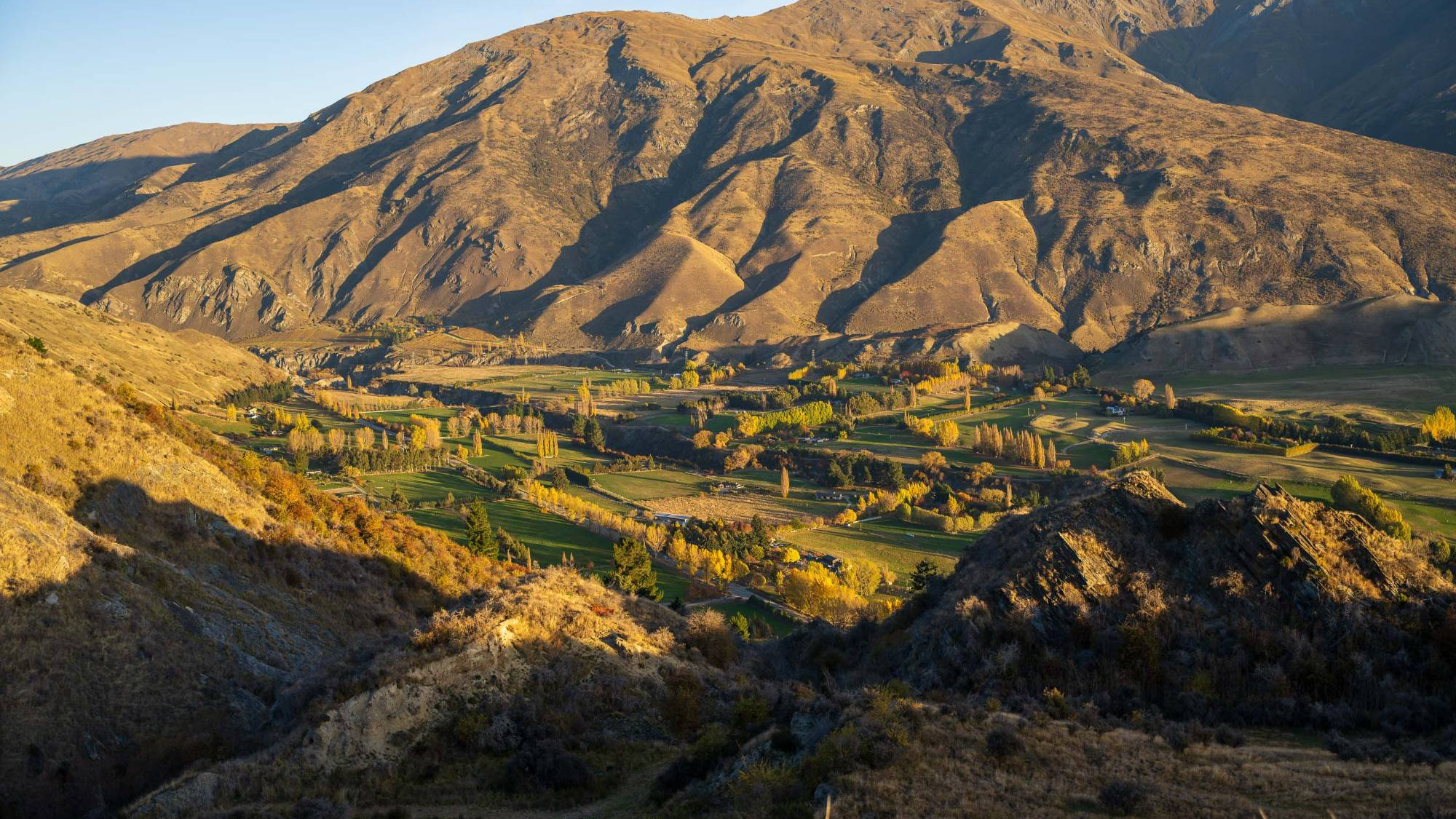 Golden hill country rising above a farmed valley floor in Central Otago