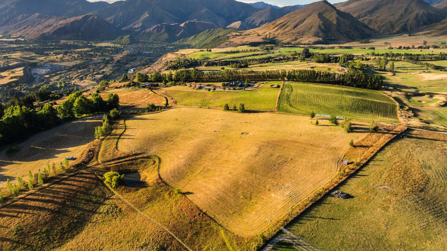 Aerial view of fenced paddocks and farmland running up to mountain ranges